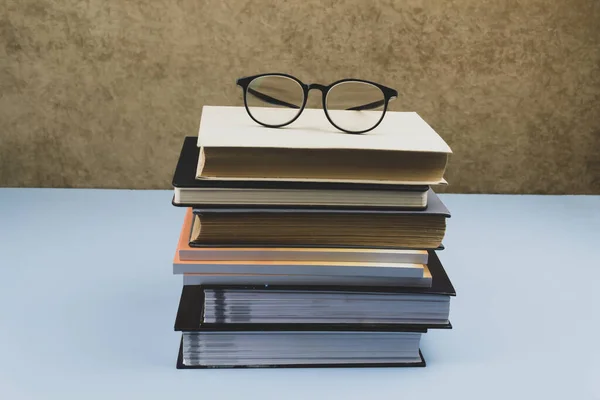 Black-rimmed glasses lie on a pile of books. Blue background