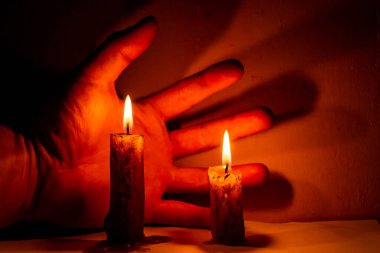 Eski bir gece odasında, arka planda elleri olan iki yanan mum.