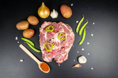 Çan biberiyle süslenmiş taze et diliminin en üst görüntüsü. Patates, soğan, sarımsak. Siyah arkaplan