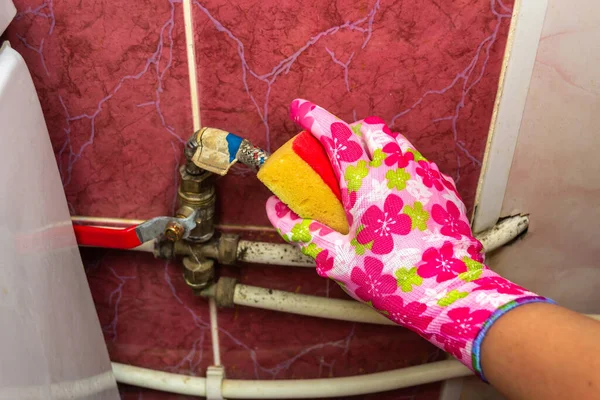 Hand in a rubber glove cleans pipes with a sponge on a background of red tiles