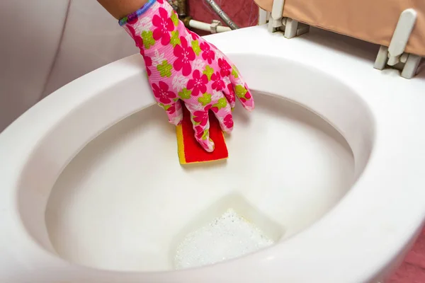 A woman\'s hand in a rubber glove cleans the toilet bowl with a brush, sink Clean your house.