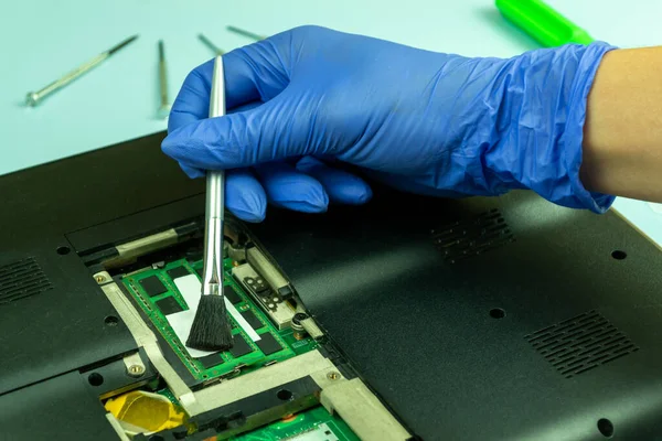 Disassembling a laptop in a repair shop. The master removes dust from the computer parts with a brush. Concept for computer equipment, repair.