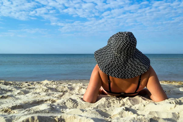Woman in black bikini relaxing on the beach wearing a hat