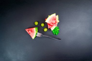 Siyah bir zemin üzerinde çatalla tutturulmuş sulu olgun kırmızı karpuz dilimleri.