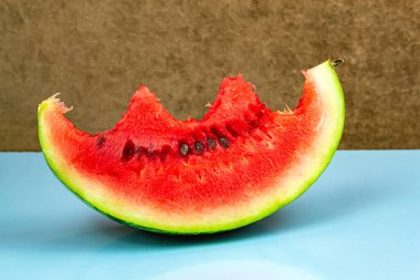 Isırılmış kırmızı sulu olgun karpuz mavi arka planda