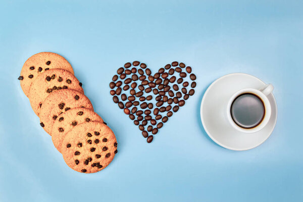Сердце из кофейных зерен, чашка кофе и печенье на синем фоне