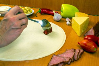 Kadın pizza hamuruna sos sürüyor, pizza malzemeleri de yakınlarda. Ahşap arkaplan