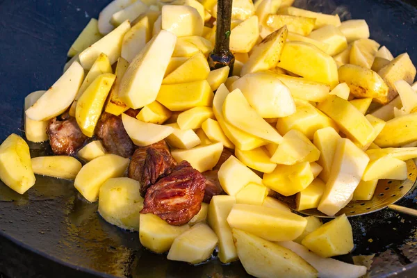 Traditional fried potatoes with pork in a skillet over a fire.