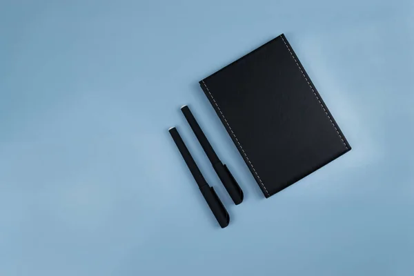 Cuaderno Negro Dos Bolígrafos Negros Acostados Junto Una Mesa Azul —  Fotos de Stock