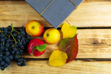 Üzüm ve elmanın yanında ahşap bir zemin üzerine gri bir kitap