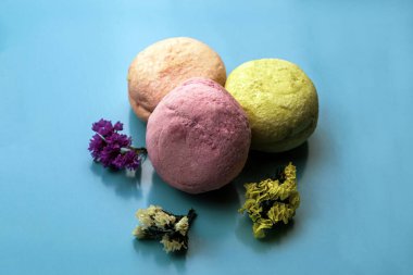 Mavi arka planda çok renkli badem kurabiyeleri, çok renkli çiçeklerin yanında.