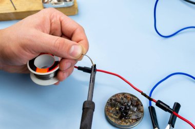 Bir adam mavi arka planda bir takviye kablosu lehimliyor. yakın plan