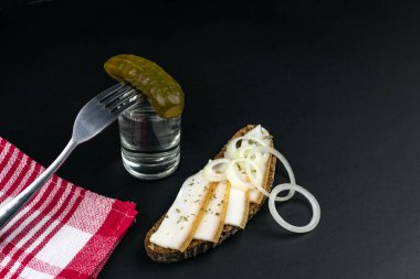 Bir bardak votka, salatalık turşusu, siyah arka planda pastırmalı iki parça ekmek.