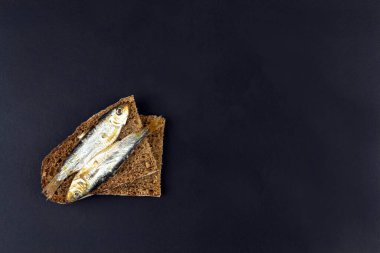 Yukarıdan siyah zemin üzerinde iki dilim ekmek ve balık.