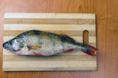 Masadaki kesme tahtasının üzerine taze balık konmuş. Temizlik için balık hazırlıyorum.