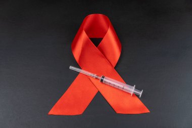 Siyah arka planda Kızıl AIDS Günü kurdelesi ve şırınga