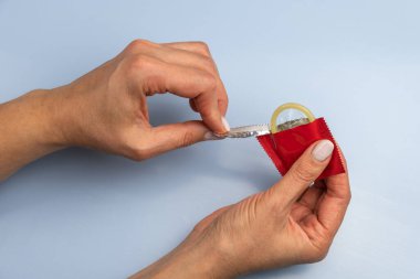 Kadın mavi arka planda prezervatif açıyor. Yakın plan.