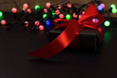 Siyah arka planda hediye kutuları, arka planda bir çelenk parlıyor. Noel ve Yeni Yıl kavramı