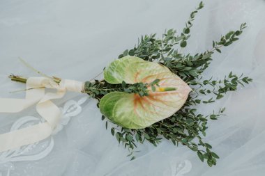 Beyaz saten kurdele ile yeşil antoryum ile olağandışı gelin buketi. Buket düğün elbise karşı yalan