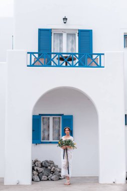 Beyaz elbiseli romantik gelin terasta poz veriyor. Arka planda dağlar ve deniz var.