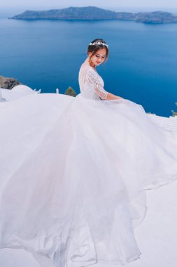 Beyaz elbiseli romantik gelin terasta poz veriyor. Arka planda dağlar ve deniz var.