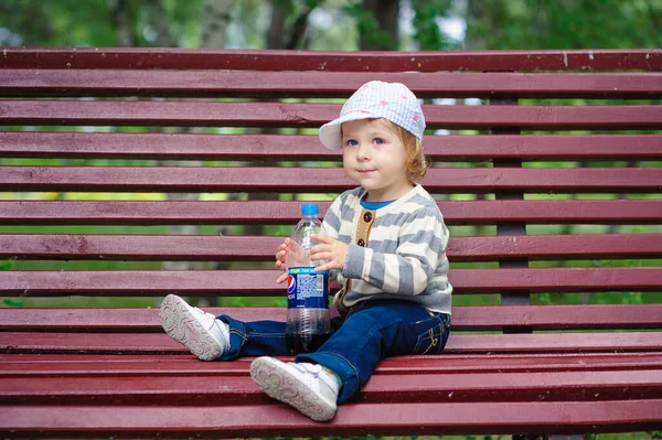 Klein meisje zittend op het bankje in park — Stockfoto