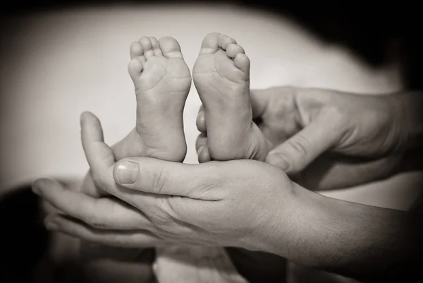 Jambes d'enfant dans les mains de la mère. Petites jambes d'un nouveau-né sur les mains féminines gros plan. Maman et son bébé. Le concept d'une famille heureuse. Concept de santé. Le traitement . — Photo