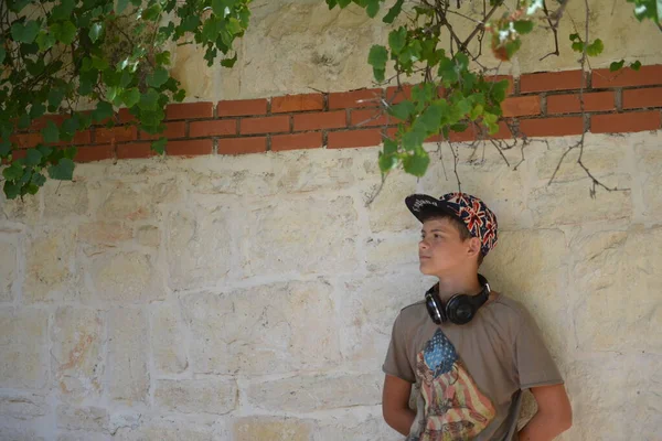Um retrato de um menino com fones de ouvido em roupas casuais posando sobre a parede de tijolo. Moda para adolescentes do sexo masculino . — Fotografia de Stock