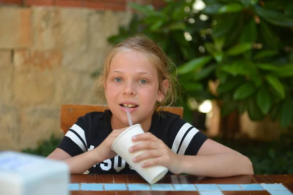 A menina bebe coquetel de leite em um café de rua. Férias de verão — Fotografia de Stock