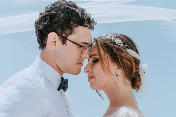 Hermosa novia y novio abrazos y besos bajo el velo nupcial en su día de la boda de verano en la isla griega Santorini — Foto de Stock