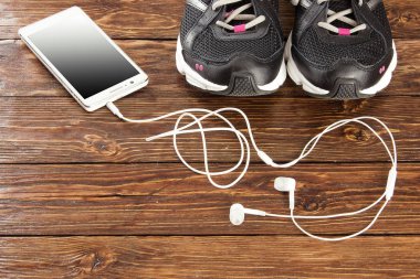 Spor ayakkabı, telefon ve kulaklık kahverengi ahşap arka plan üzerinde