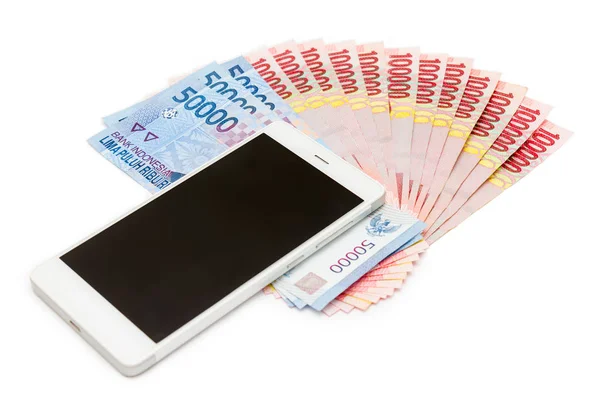 Smartphone above the piles of Indonesia Rupiah (IDR) banknotes on the white isolated background.