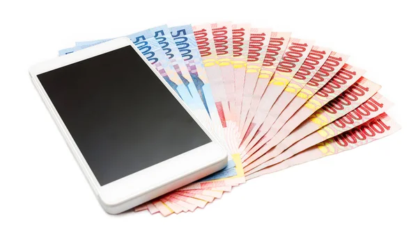 Smartphone above the piles of Indonesia Rupiah (IDR) banknotes on the white isolated background.