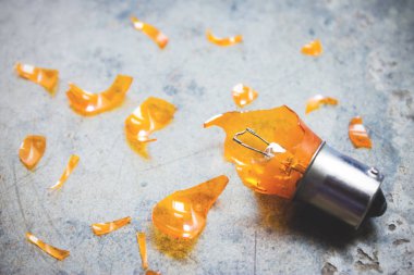 Otomotiv ampul kırık durumda ve keskin cam kırıkları çevresinde dokulu arka plan üzerinde dağınık.