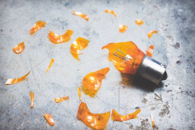 Otomotiv ampul kırık durumda ve keskin cam kırıkları çevresinde dokulu arka plan üzerinde dağınık.