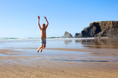 Teenagers having fun at Praia de Odeceixe in south Portugal. Happy children playing, splashing and swimming in the ocean at one of the most beautiful beaches in Algarve region. clipart