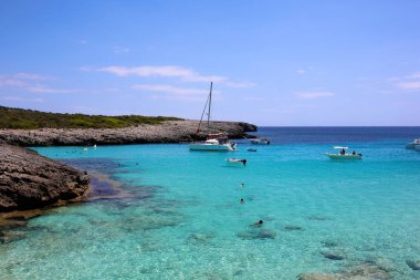 Cala Es Talaier, Minorca, Balear Adası, İspanya güzel koyunda. Yelkenli tekneler ve turkuaz deniz suda yüzen insanlar. Yaz aile tatil için mükemmel bir yer.