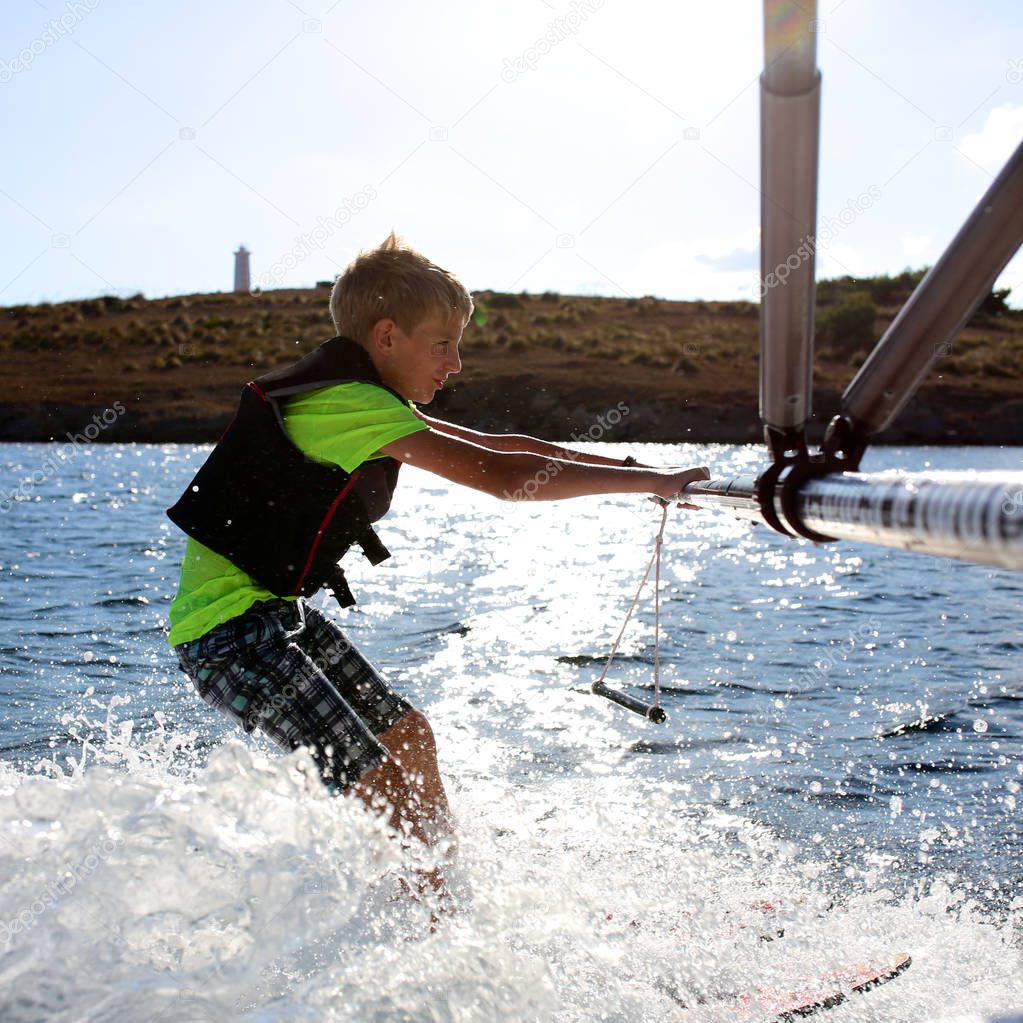 Young sportive teenage boy waterskiing from the boat. Adventurous summer holidays at the sea. Water sport activity on the beach.