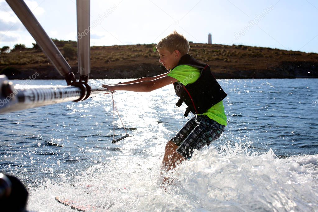 Young sportive teenage boy waterskiing from the boat. Adventurous summer holidays at the sea. Water sport activity on the beach.