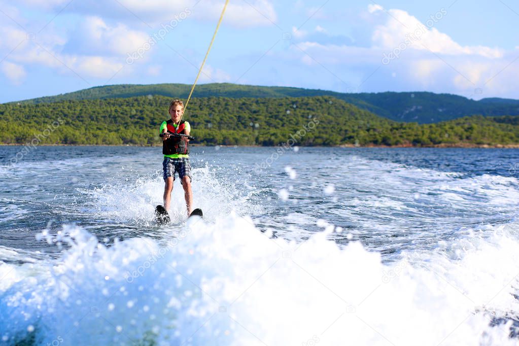 Young sportive teenage boy waterskiing from the boat. Adventurous summer holidays at the sea. Water sport activity on the beach.