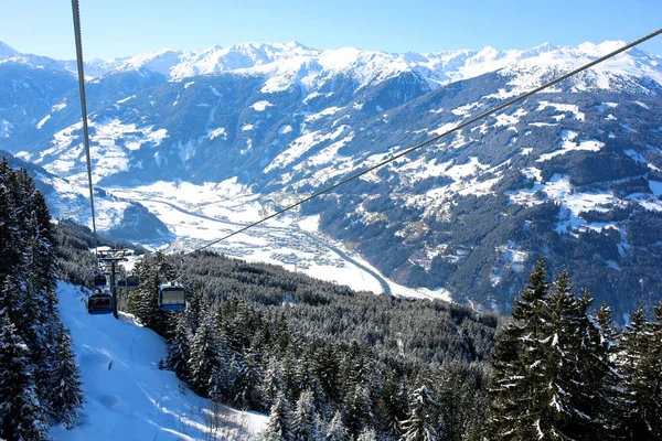 Modern comfortable gondola lift in Alpine ski resort. People enjoying skiing on prepared slopes in the Alps on sunny day. Beautiful snowy trees and little village in the mountains. Perfect winter holidays destination for family.