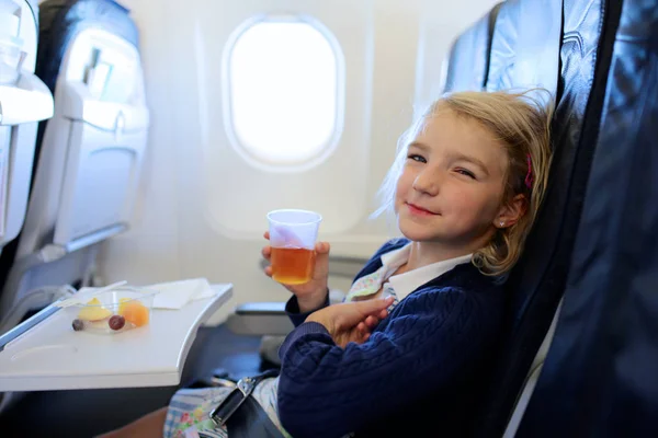 飛行機でリラックスして食事を楽しんで幸せな小さな女の子 家族の休日の行先に飛行機で旅行です 子供友好的な航空会社 — ストック写真