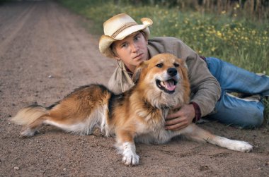 kovboy şapkalı adam köpeğini bir ülke yolda hugs.