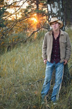 gün batımında sonbahar ormandaki kovboy kıyafetli genç adam