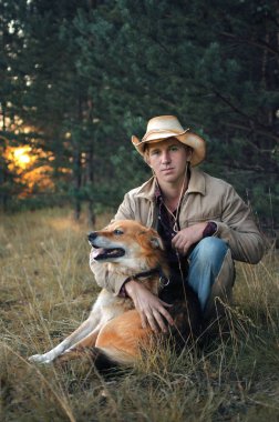 kovboy elbiseli Genç adam köpeğini tatile ormanın kenarında oturan hugs