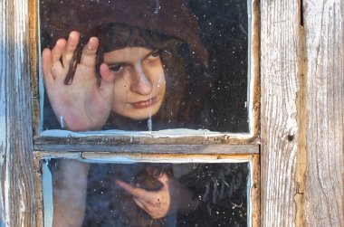 Yün içinde sarılı Gözlerinin altındaki morluklar kadınla ne yazık ki görünüyor eski bir kulübe, eski püskü pencerede avucunun ile cam dokunmak ve pencere dışında belli ki soğuk üzgün, o gibi görünüyor