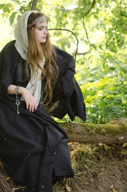 Genç kadın, belki de bir cadı siyah giysiler ve beyaz şal oturur ve güneşli bir günde bahçede bir ağaç dalı dayanmaktadır