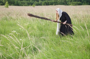 cadı bir süpürge ile yoğun çim ile büyümüş bir yeşil alan üzerinde dolaşır
