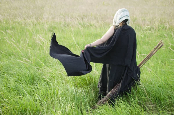 巫婆在黑色的礼服和白色手帕与扫帚穿过田野之间的高大草丛 挥舞着她的服装 — 图库照片