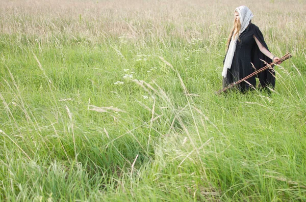 ほうきで魔女が密度の高い草の生い茂った緑のフィールドにさまよう — ストック写真